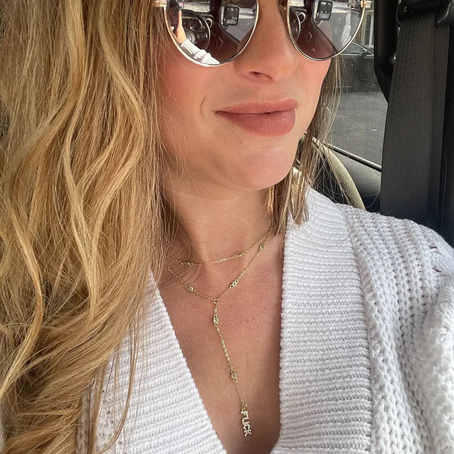 Woman wearing gold necklace, sunglasses and a white cardigan inside a vehicle